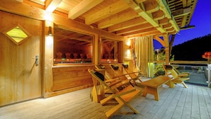 A wooden deck with lounge chairs and a glass enclosure with a view. - Tanne Tonbach - Wellness & Wohlfühl Hotel (Baiersbronn)