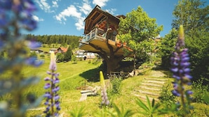 A treehouse with a balcony, surrounded by greenery and houses. - Tanne Tonbach - Wellness & Wohlfühl Hotel (Baiersbronn)