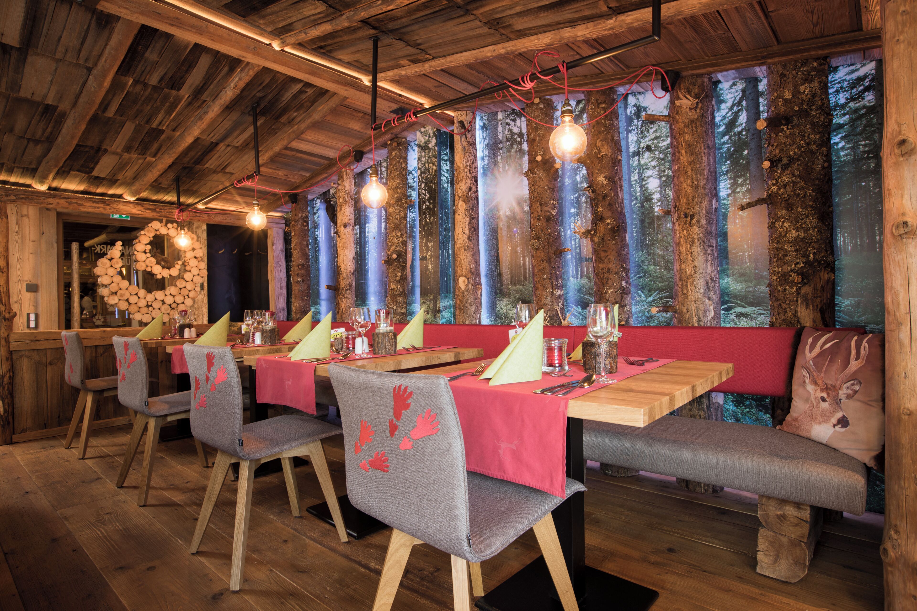 A restaurant with wooden interior, tables with pink tablecloths, and a forest view.