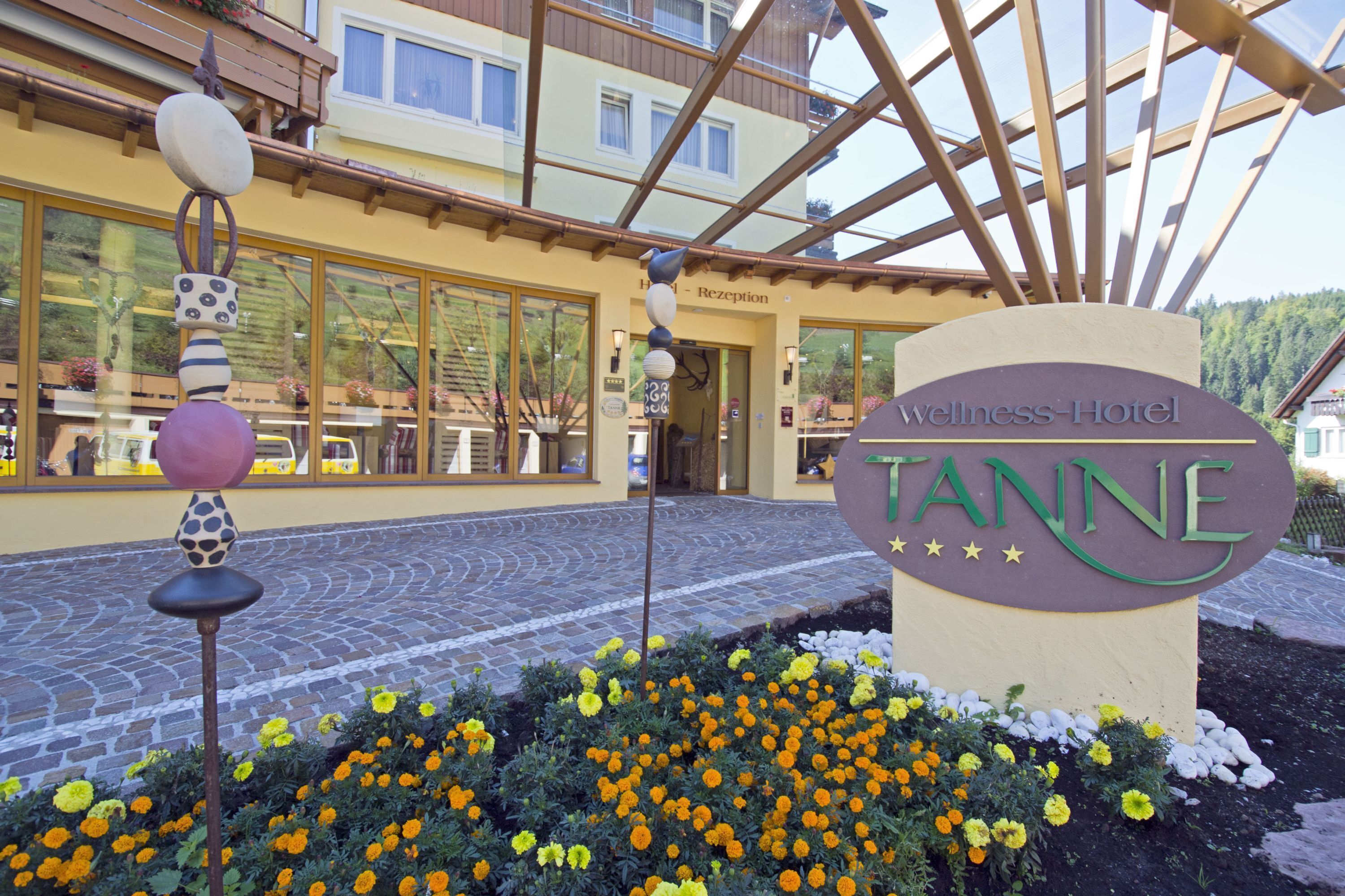 Ein Hotel Eingang mit einem Schild, auf dem 'Wellness Hotel Tanne' steht, und einem Blumenbeet davor.