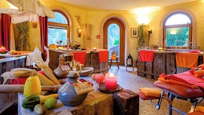 A spa room with a wooden bench, a massage table, a window with a view of greenery, and various spa amenities. - Tanne Tonbach - Wellness & Wohlfühl Hotel (Baiersbronn)