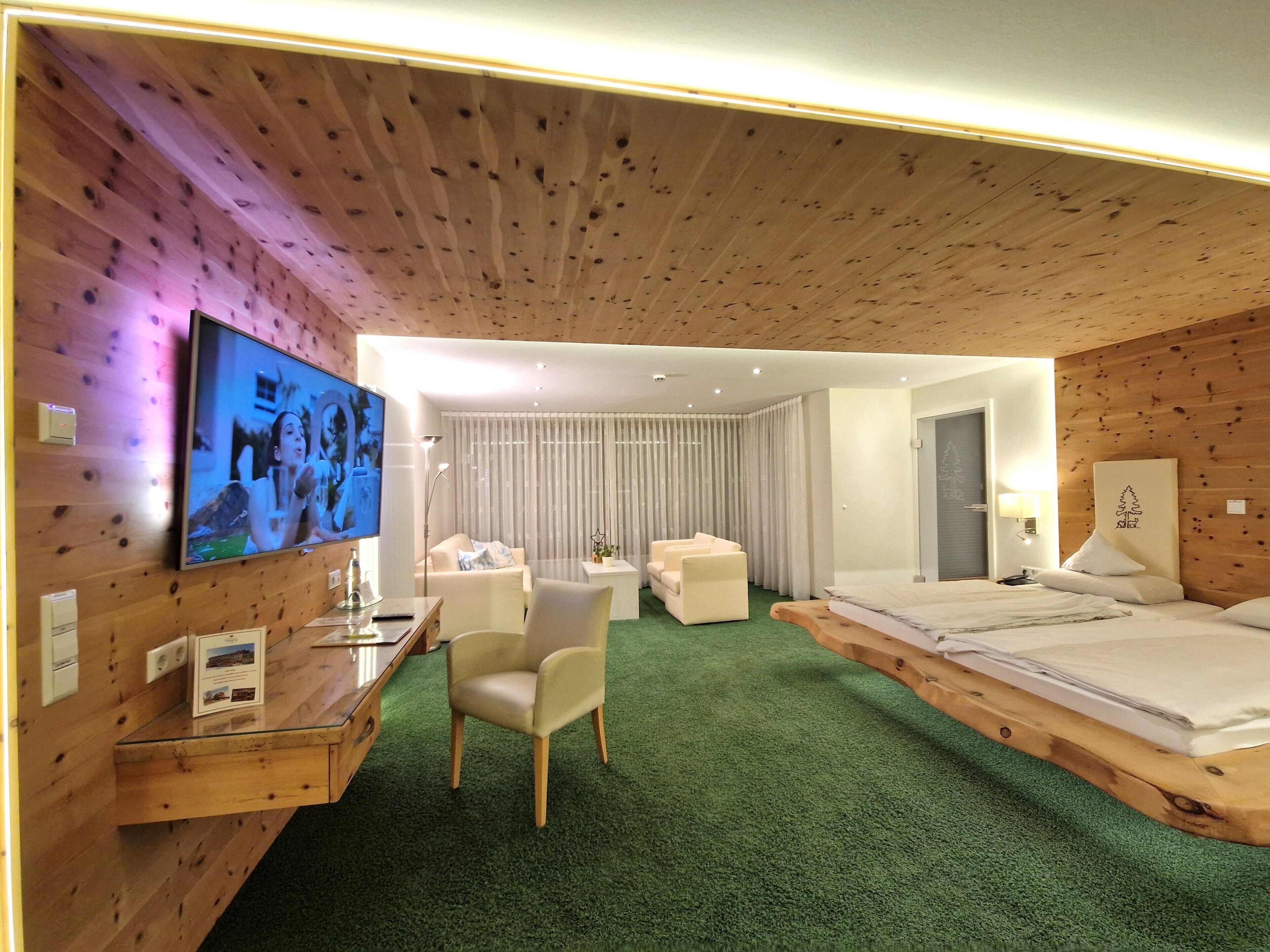 Ein Hotelzimmer mit Holzboden, einem Bett, einem Schreibtisch mit Fernseher, einem Stuhl und einem grünen Teppich.