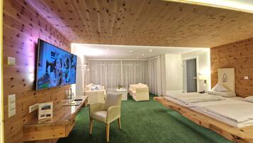 Ein Hotelzimmer mit Holzboden, einem Bett, einem Schreibtisch mit Fernseher, einem Stuhl und einem grünen Teppich.