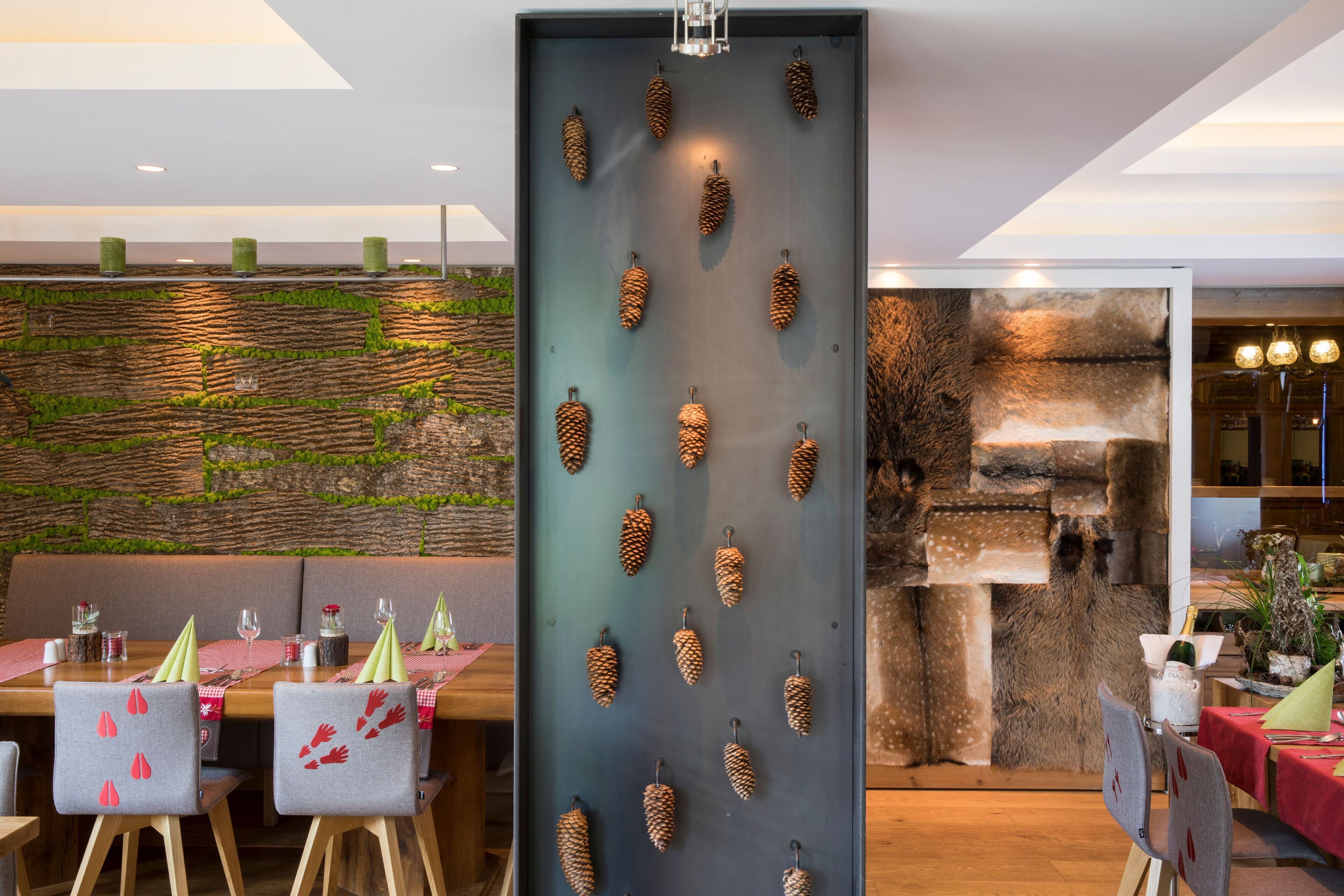 Ein Restaurant mit Holztischen und -stühlen, einer Wand mit grünen Pflanzen und einer Wanddekoration aus Tannenzapfen.
