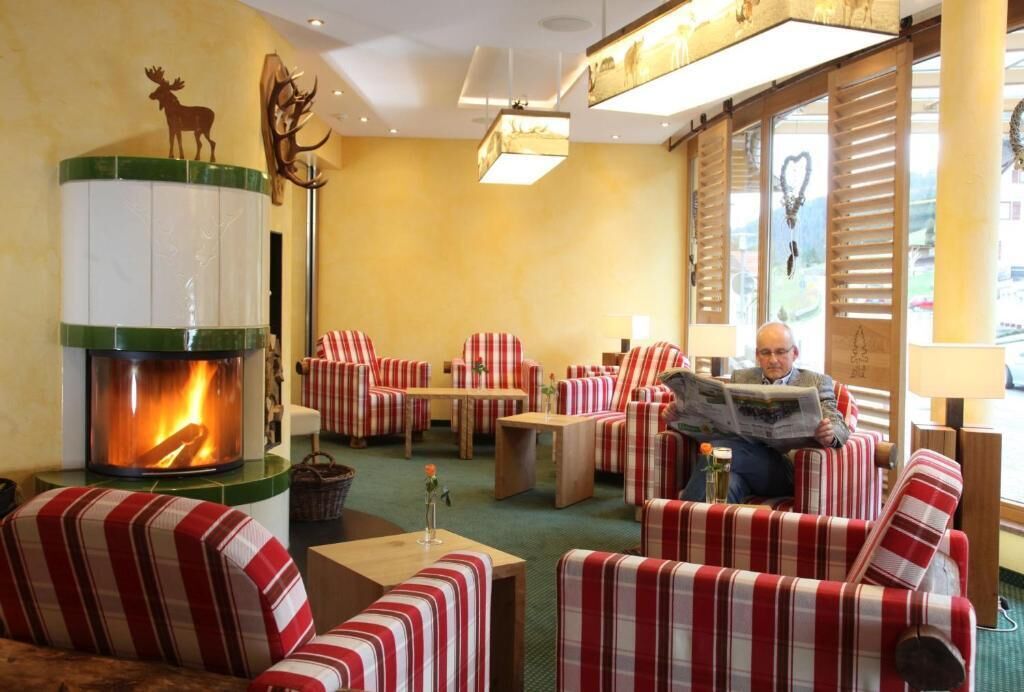 A cozy lounge area with striped sofas and armchairs, a fireplace, and a large window with shutters.