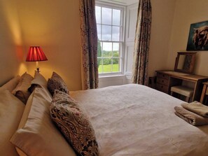 A bedroom with a large bed, a desk, and a window with curtains.