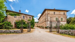 A rural street with stone buildings, a gate, and potted plants. - Apartment at Tenuta Bichi Borghesi Farm (Monteriggioni)