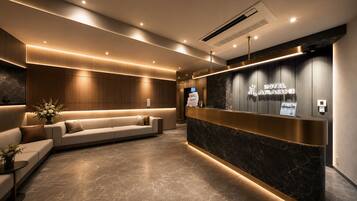 A modern hotel reception area with a reception desk, a sofa, and a wall-mounted TV.