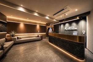 A modern hotel reception area with a reception desk, a sofa, and a wall-mounted TV.
