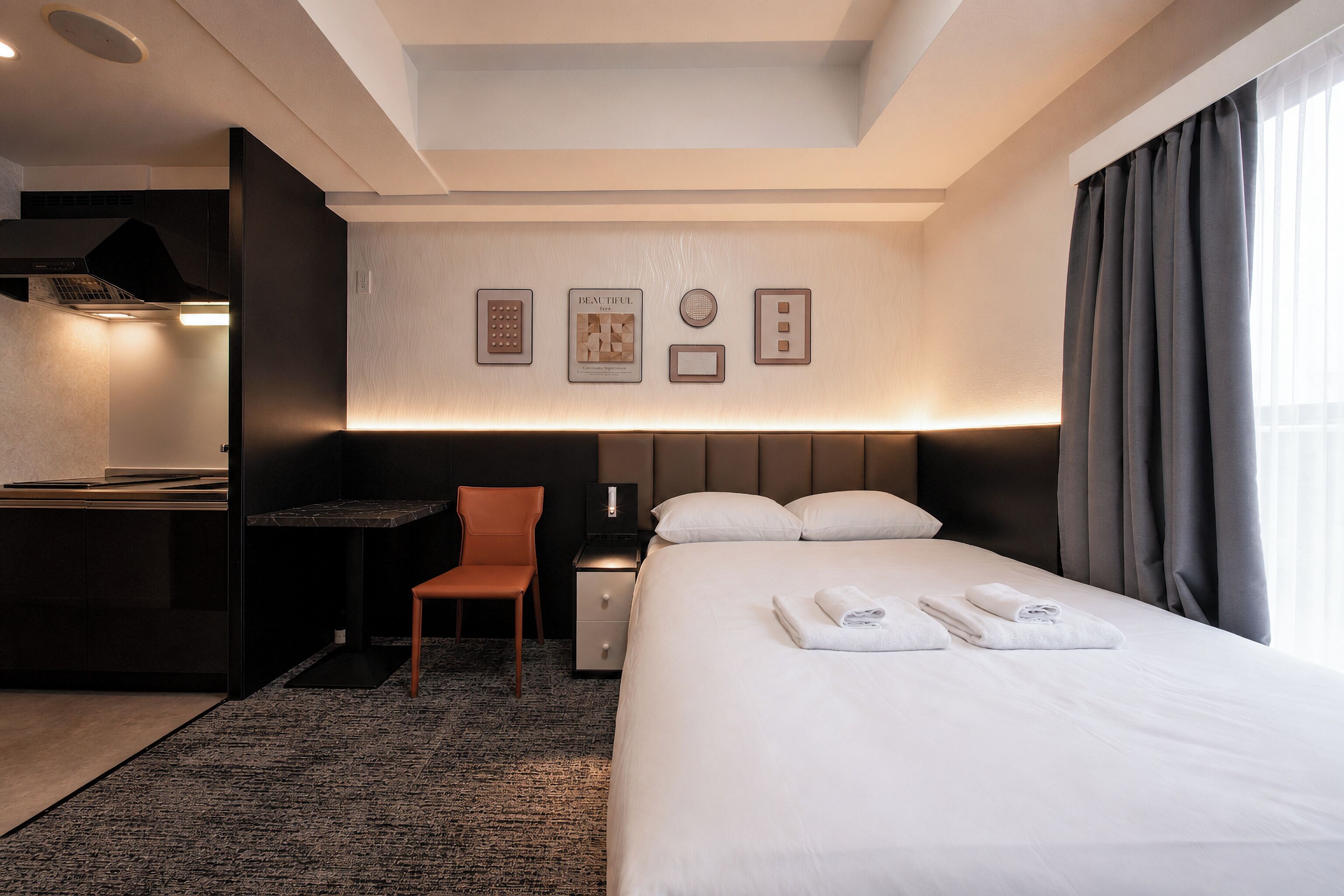 A hotel room with a bed, a desk, a chair, a nightstand, and a wall with framed pictures.