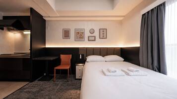 A hotel room with a bed, a desk, a chair, a nightstand, and a wall with framed pictures.