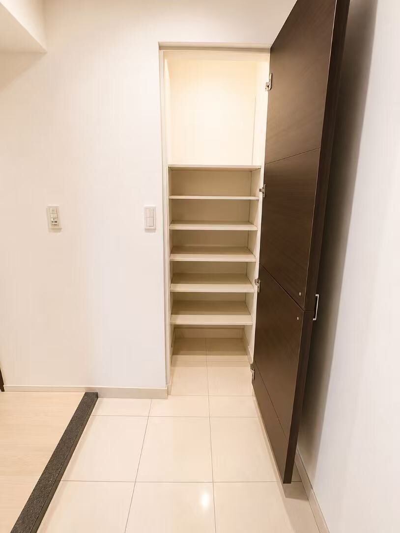 A hallway with a closet containing multiple shelves and a door.