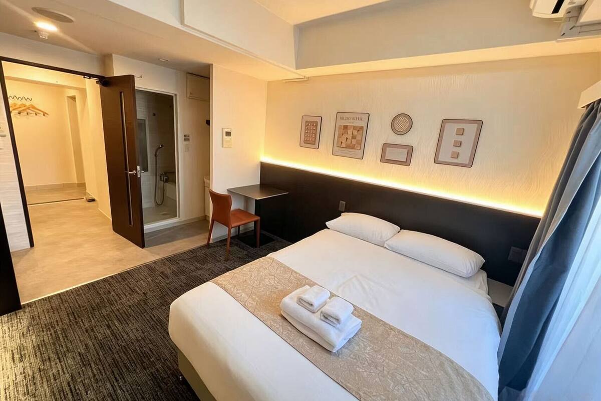 Una habitación de hotel con cama, escritorio, silla y zona de ducha.