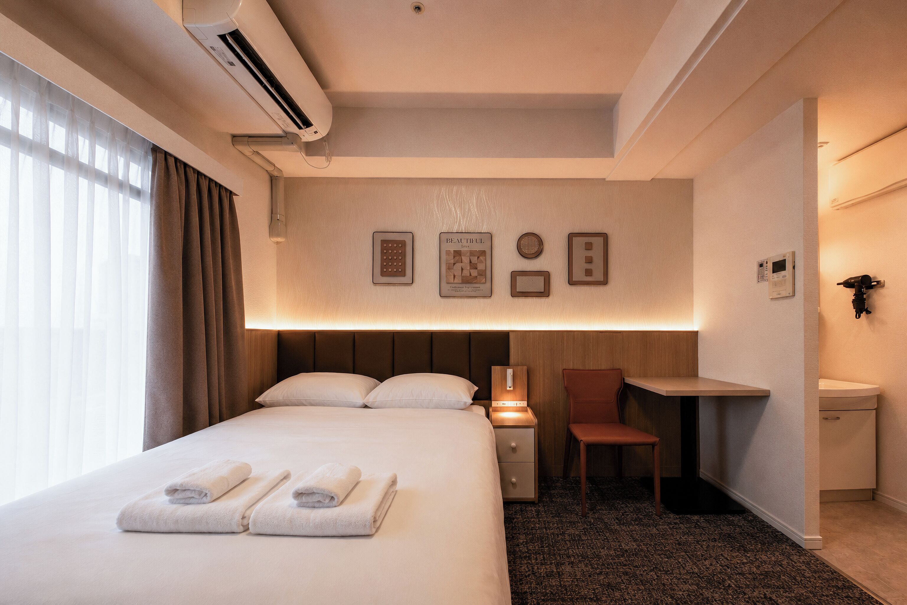 Habitación de hotel con cama, escritorio, silla, mesita de noche y aire acondicionado de pared.