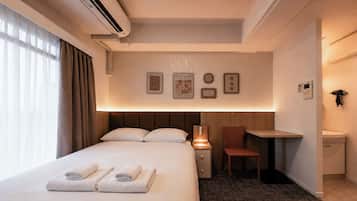 Habitación de hotel con cama, escritorio, silla, mesita de noche y aire acondicionado de pared.