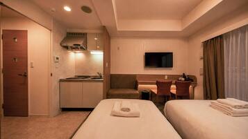 A hotel room with two beds, a kitchenette, a desk, a TV, and a bathroom.