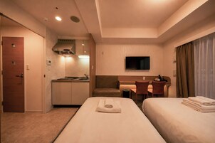 Ein Hotelzimmer mit zwei Betten, einer Küchenzeile, einem Schreibtisch, einem Fernseher und einem Badezimmer.