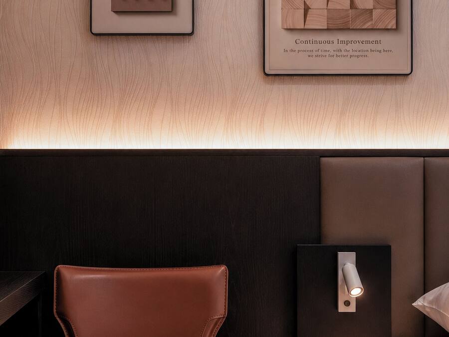 A modern bedroom with a brown leather chair, a bedside table with a lamp, and framed artwork on the wall.