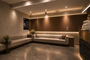 Un área de recepción moderna con un sofá modular, una mesa de recepción y un espejo montado en la pared.