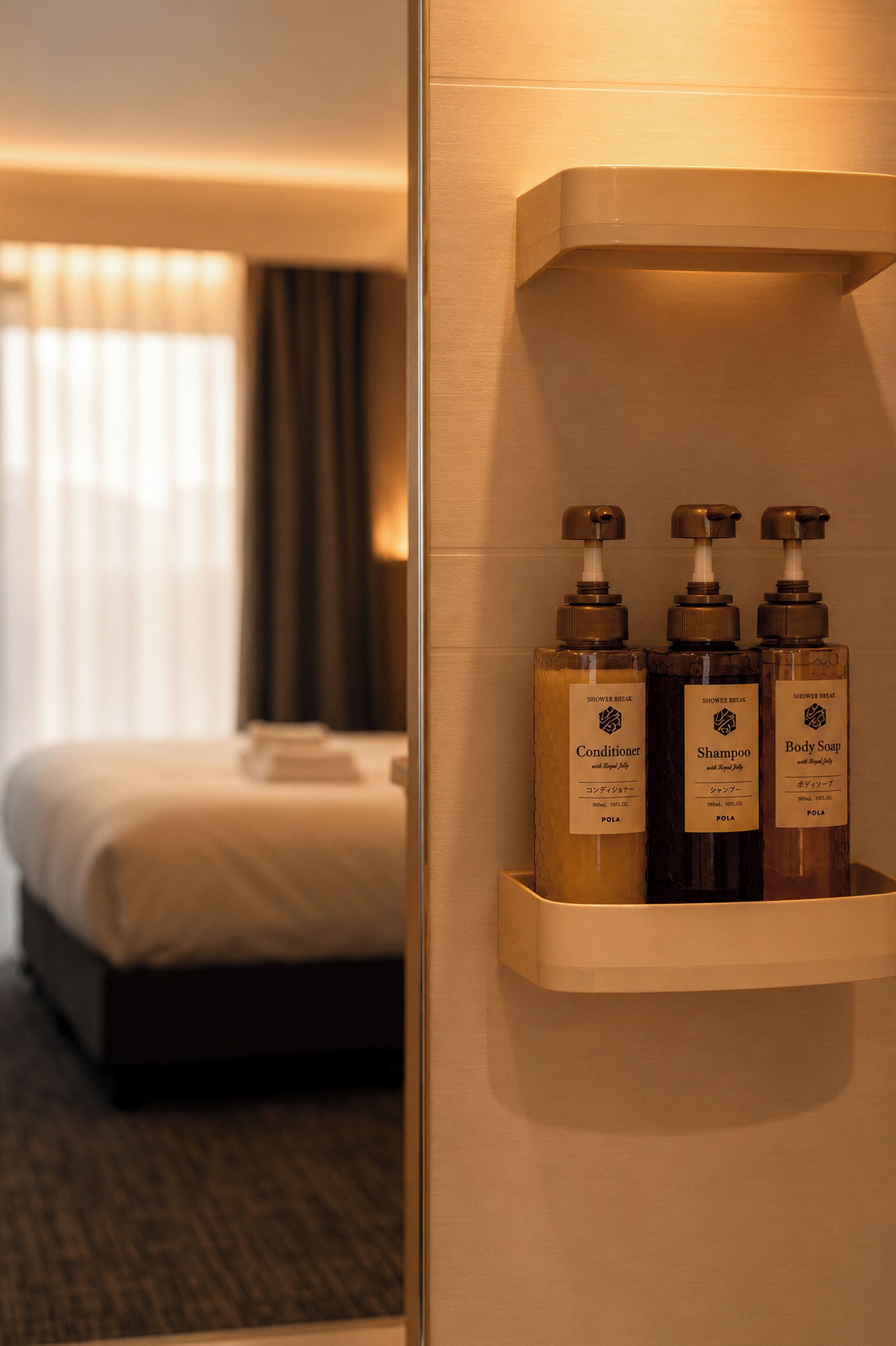 A hotel room with a bed, a nightstand, and a shelf with three toiletries.