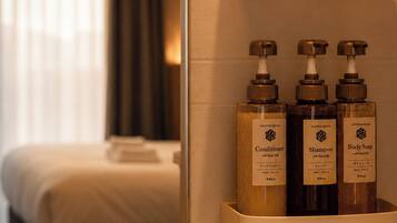 A hotel room with a bed, a nightstand, and a shelf with three toiletries.