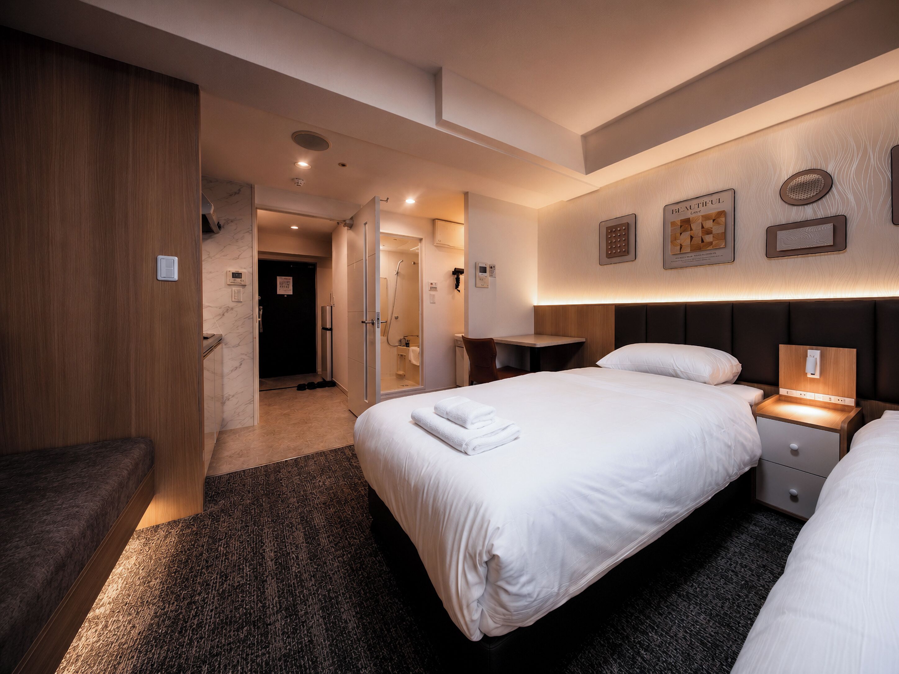 Hotellihuone, jossa on sänky, yöpöydät, työpöytä, suihkutila ja ovi, joka johtaa toiseen huoneeseen.