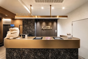 A reception desk with a plush toy, a digital screen, and a sign indicating the hotel's name.