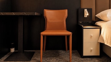 Une chambre d’hôtel moderne avec un fauteuil en cuir, une table de chevet avec une lampe et un lit recouvert d’une couette blanche.