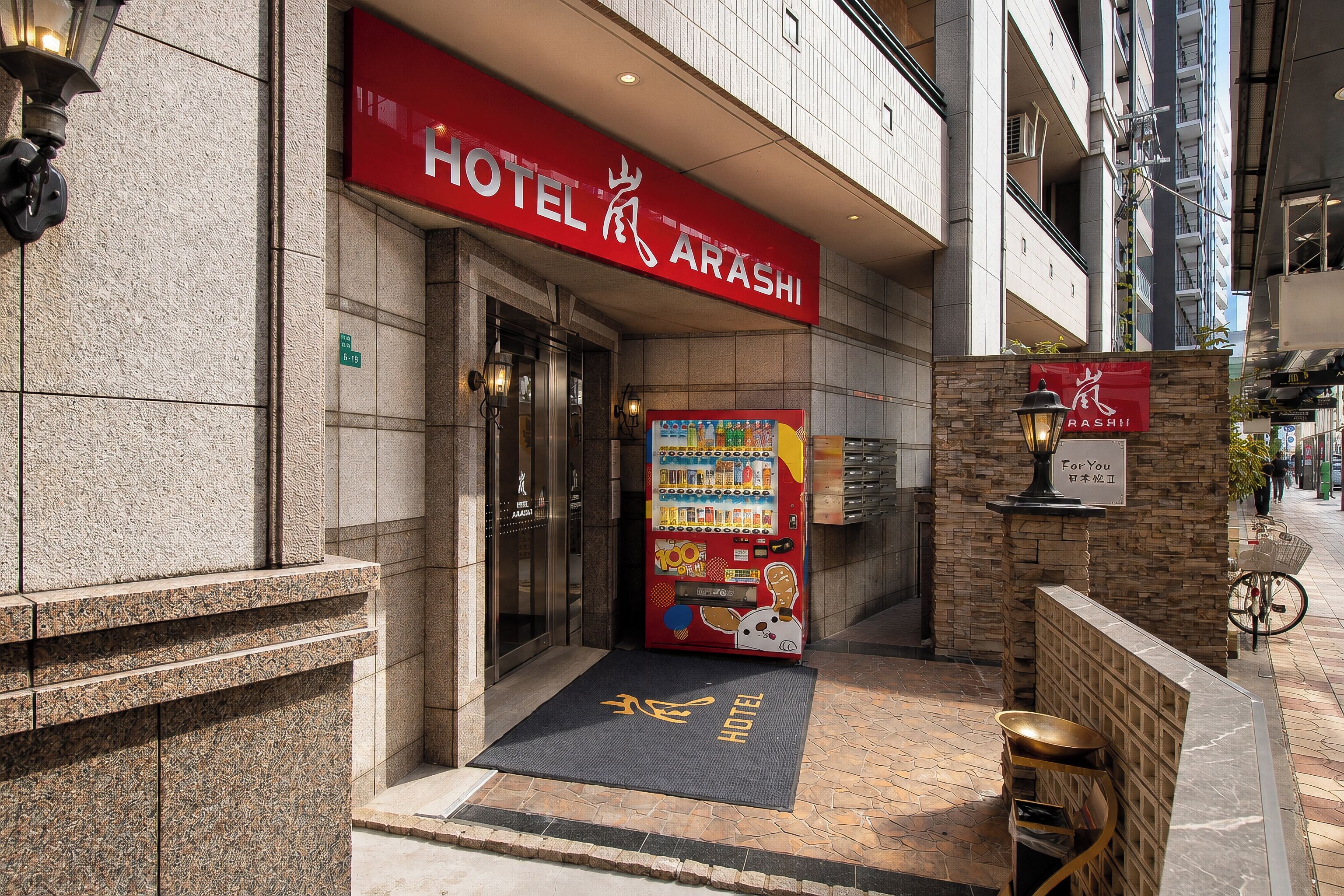 A hotel entrance with a red sign, a vending machine, and a bicycle parked outside.