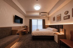 A hotel room with a bed, a desk, a TV, and a seating area.