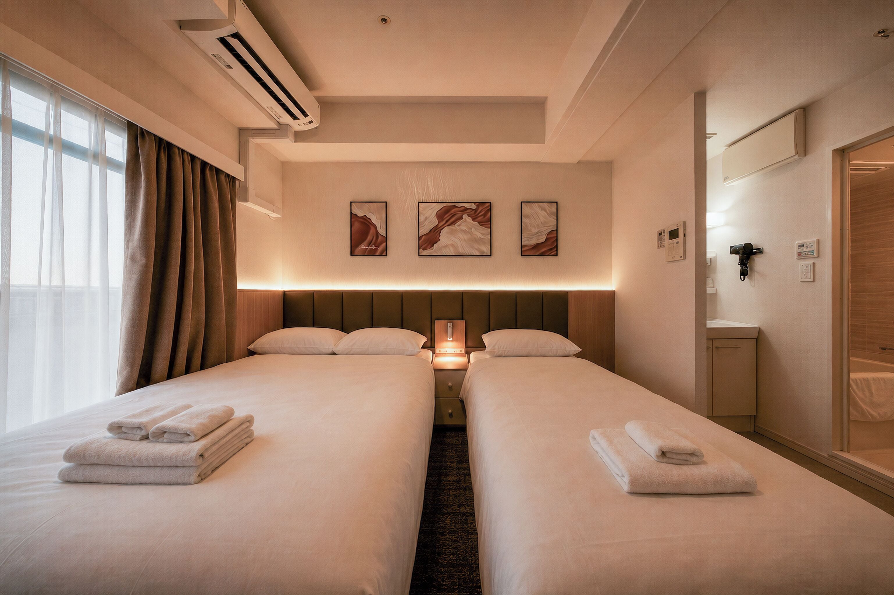 Une chambre d’hôtel avec deux lits, une table de chevet, un miroir et des œuvres d’art accrochées au mur.