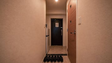 Un pasillo estrecho con una puerta al final, un aplique en la pared y un juego de felpudos negros en el suelo.