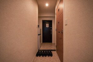 Un pasillo estrecho con una puerta al final, un aplique en la pared y un juego de felpudos negros en el suelo.