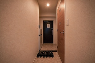 Un couloir étroit, avec une porte au fond, un luminaire fixé au mur et un ensemble de paillassons noirs sur le sol.