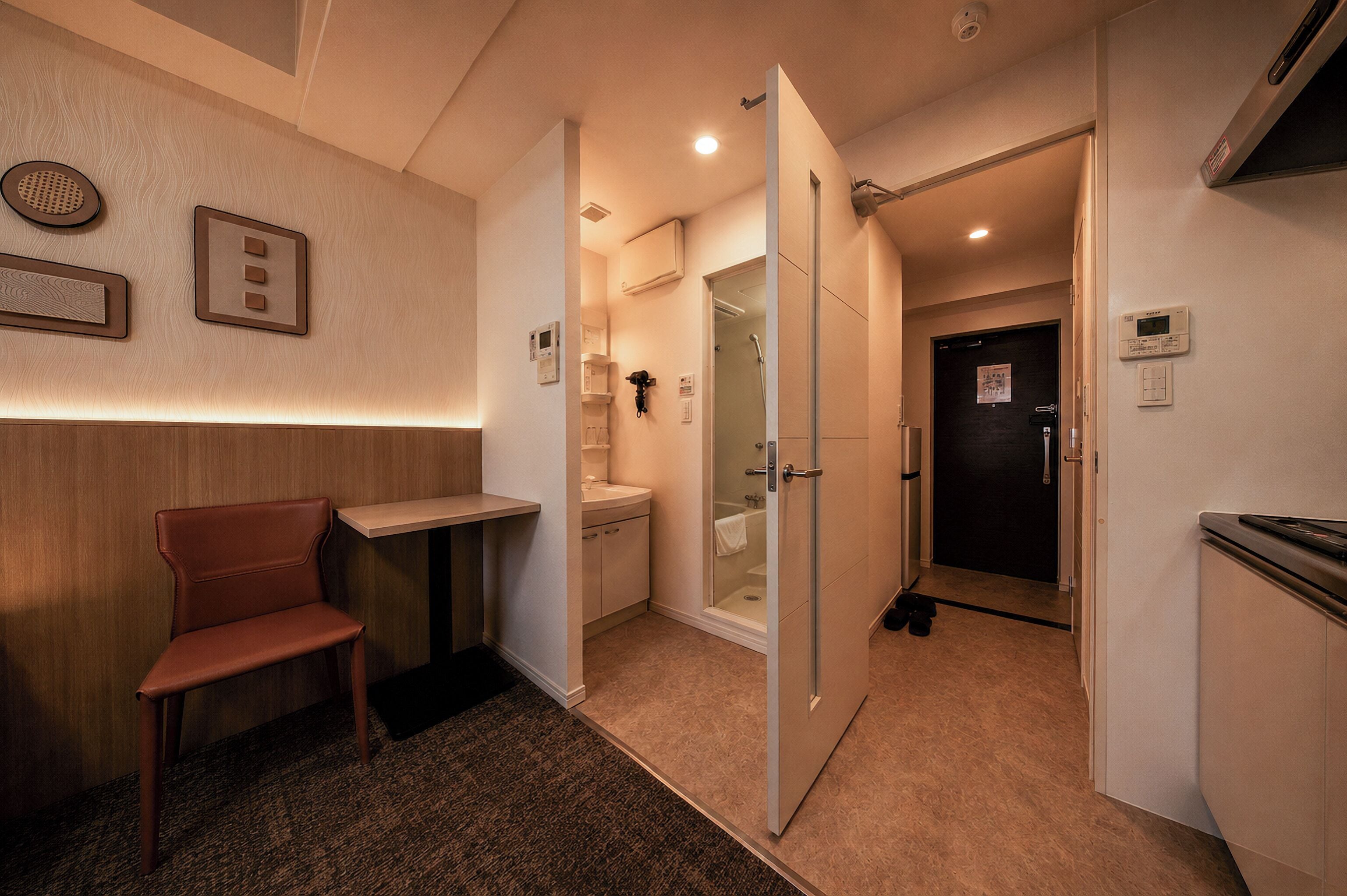 A hotel room with a wooden bench, a small table, a shower area, and a door leading to another room.