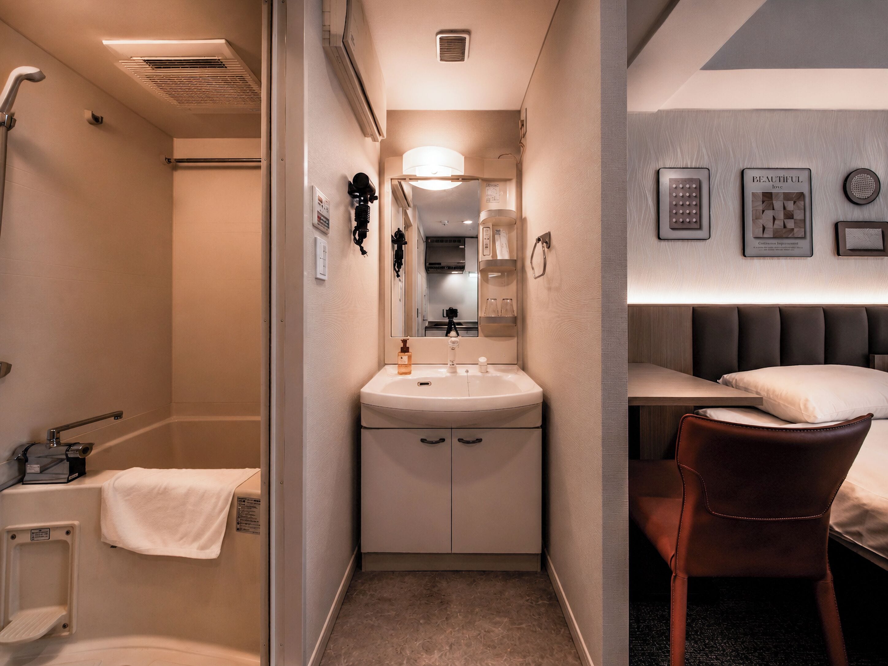 Une petite salle de bain d’hôtel comprenant une douche, un lavabo et un lit avec une tête de lit.