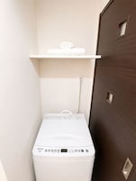 Een kleine wasruimte met een witte wasmachine en een plank erboven.