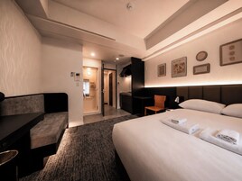 A hotel room with a bed, a sofa, a desk, and a bathroom visible through an open door.