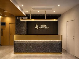 Un comptoir d’accueil surmonté d’une enseigne indiquant « RÉCEPTION » et, sur le mur, l’inscription « HÔTEL ARASHI ».