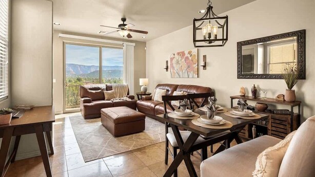 A spacious living room with a large window, a ceiling fan, a dining area with a table set for four, and a view of mountains. - Sedona Getaway Sedona! 2-King, Hiking, Views, Pets! (Sedona)