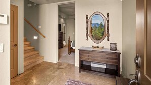 A hallway with a wooden staircase, a wooden bench with drawers, a mirror with a landscape painting, and a door on the right. - Sedona Getaway Sedona! 2-King, Hiking, Views, Pets! (Sedona)