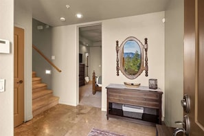 A hallway with a wooden staircase, a wooden bench with drawers, a mirror with a landscape painting, and a door on the right. - Relaxing Sedona Hiking HQ, View, West Sedona! Star (Sedona)