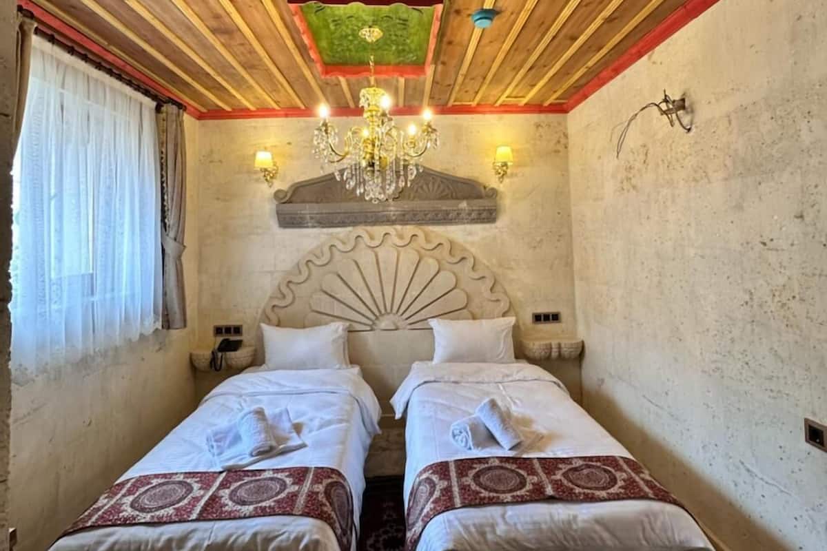 Una habitación con dos camas, una araña y una ventana con cortinas.