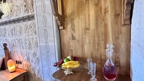 Eine rustikale Holzwand mit Steinoptik, ein kleiner Tisch mit Obstschale, zwei Gläser und eine pinkfarbene Flasche.