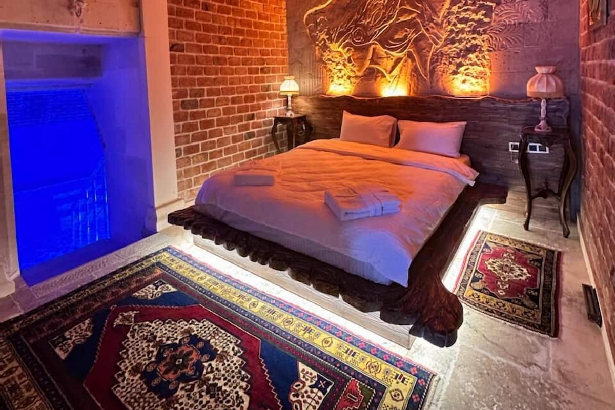 Una habitación con pared de ladrillo, cama con cabecera, candelabro, mesita de noche y alfombra estampada.