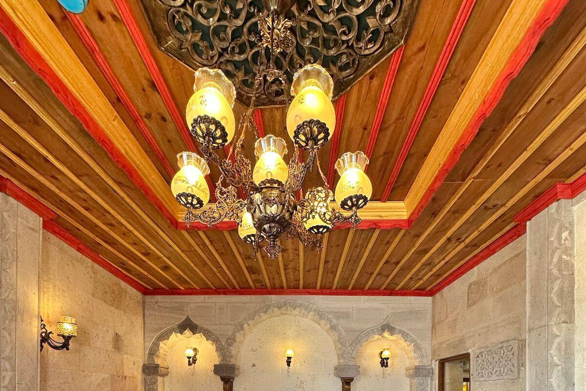 Una habitación tradicional con techo de madera, un candelabro ornamentado y una cama grande con colcha roja y blanca.
