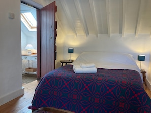 A bedroom with a bed, two bedside lamps, a skylight, and a wooden floor.