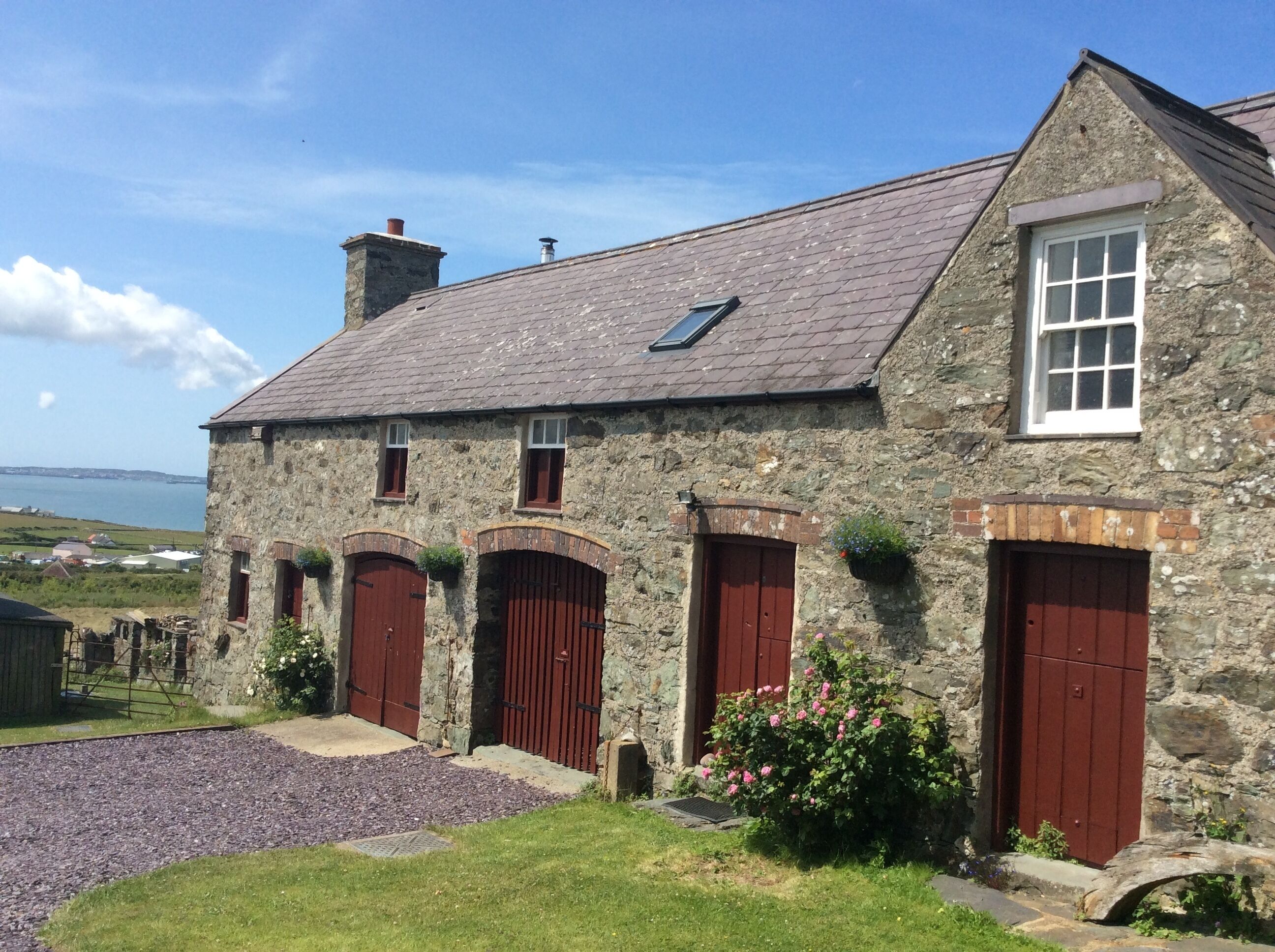 A stone building with three red doors, a small window, and a view of the sea.