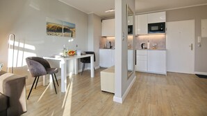 Una cocina moderna con armarios blancos, microondas y cafetera. Cuenta con una zona de comedor con mesa y sillas blancas.