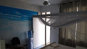 A bedroom with a bed, a desk, a chair, a water dispenser, and a large window with curtains. - Kisiwa Boutique Hotel Mombasa (Mombasa)